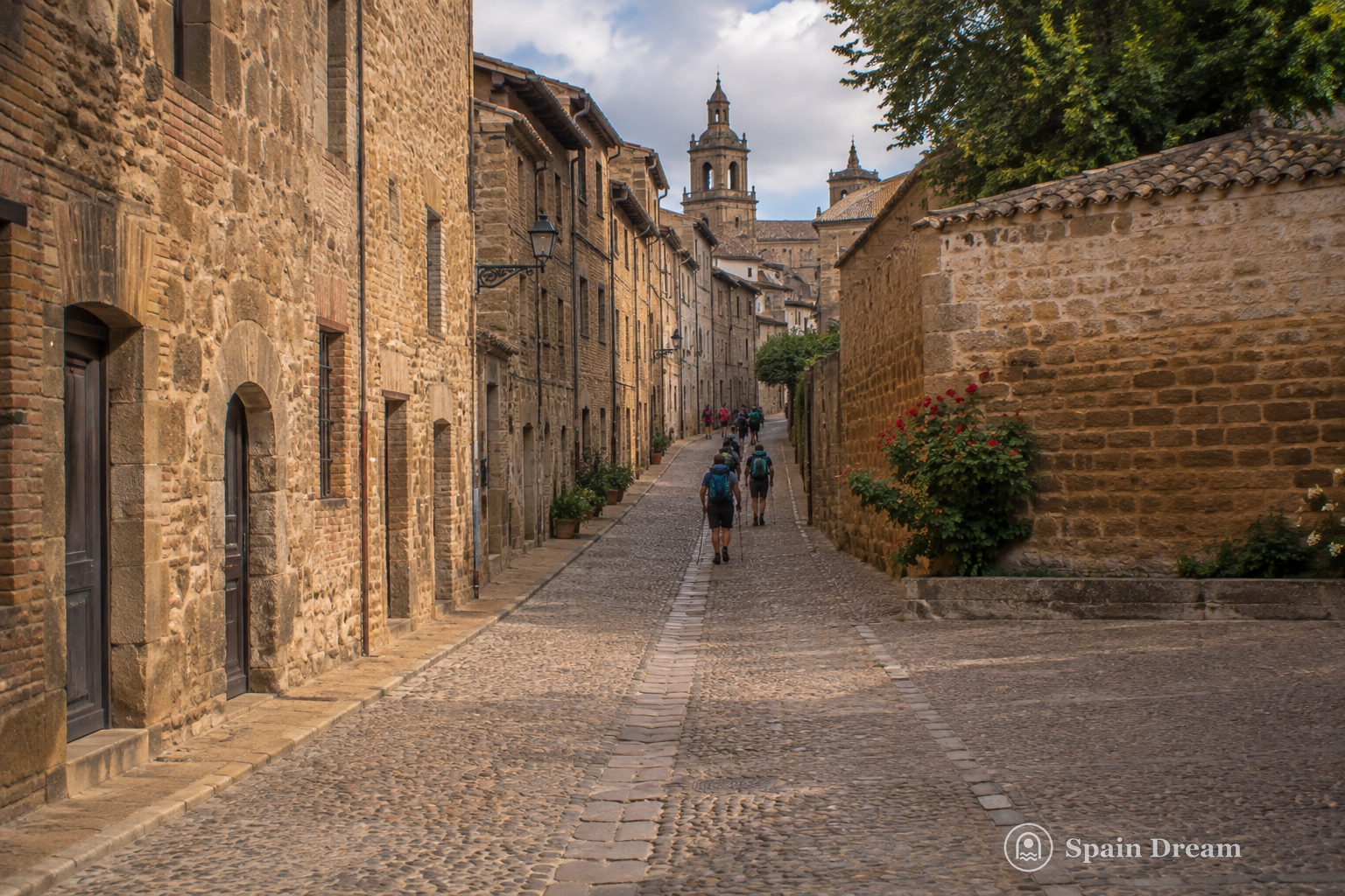 Мощёная улица Camino de Santiago в Санто-Доминго-де-ла-Кальсада с каменными домами и паломниками вдали